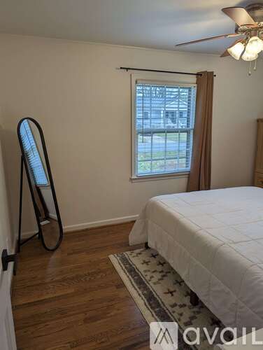 A room with a bed, a fan, and a window with a view of a building outside.