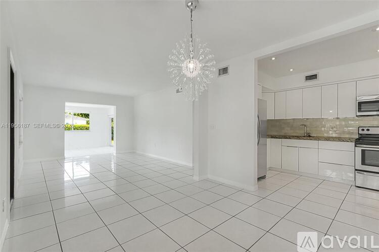 A spacious kitchen with white tiled floors and a chandelier hanging from the ceiling.