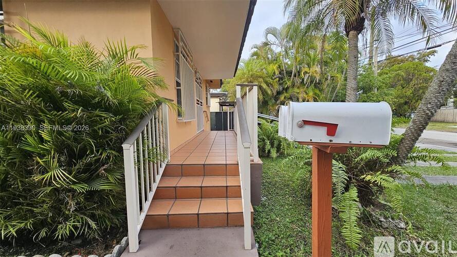 A white mailbox is on a wooden post in front of a house with a tiled staircase.