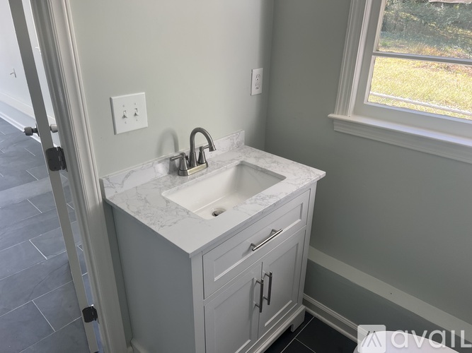 A bathroom sink with a marble countertop and white cabinetry.