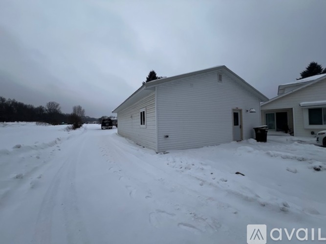 A house in the snow with a trash can outside.