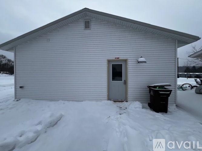 A small house with a grey door and a black trash can in front of it.
