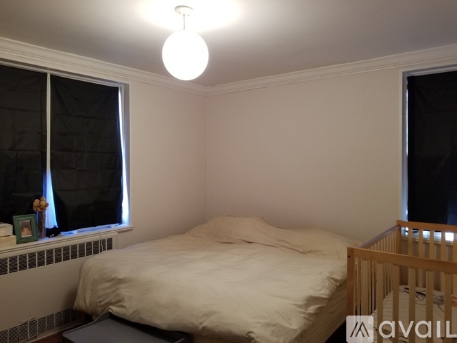 A bedroom with a bed, a window with black curtains, and a lit ceiling light.