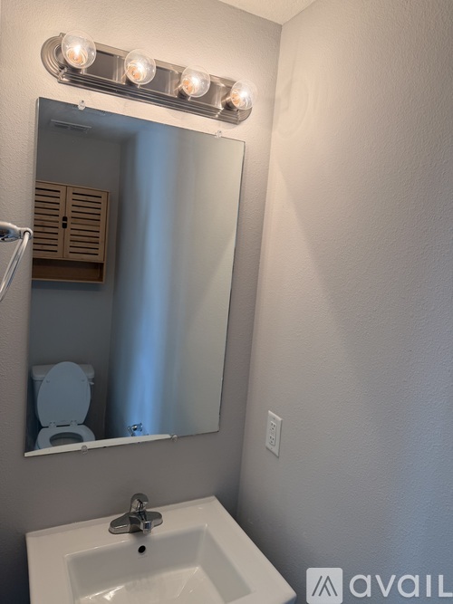 A bathroom with a white sink and a mirror with lights above it.