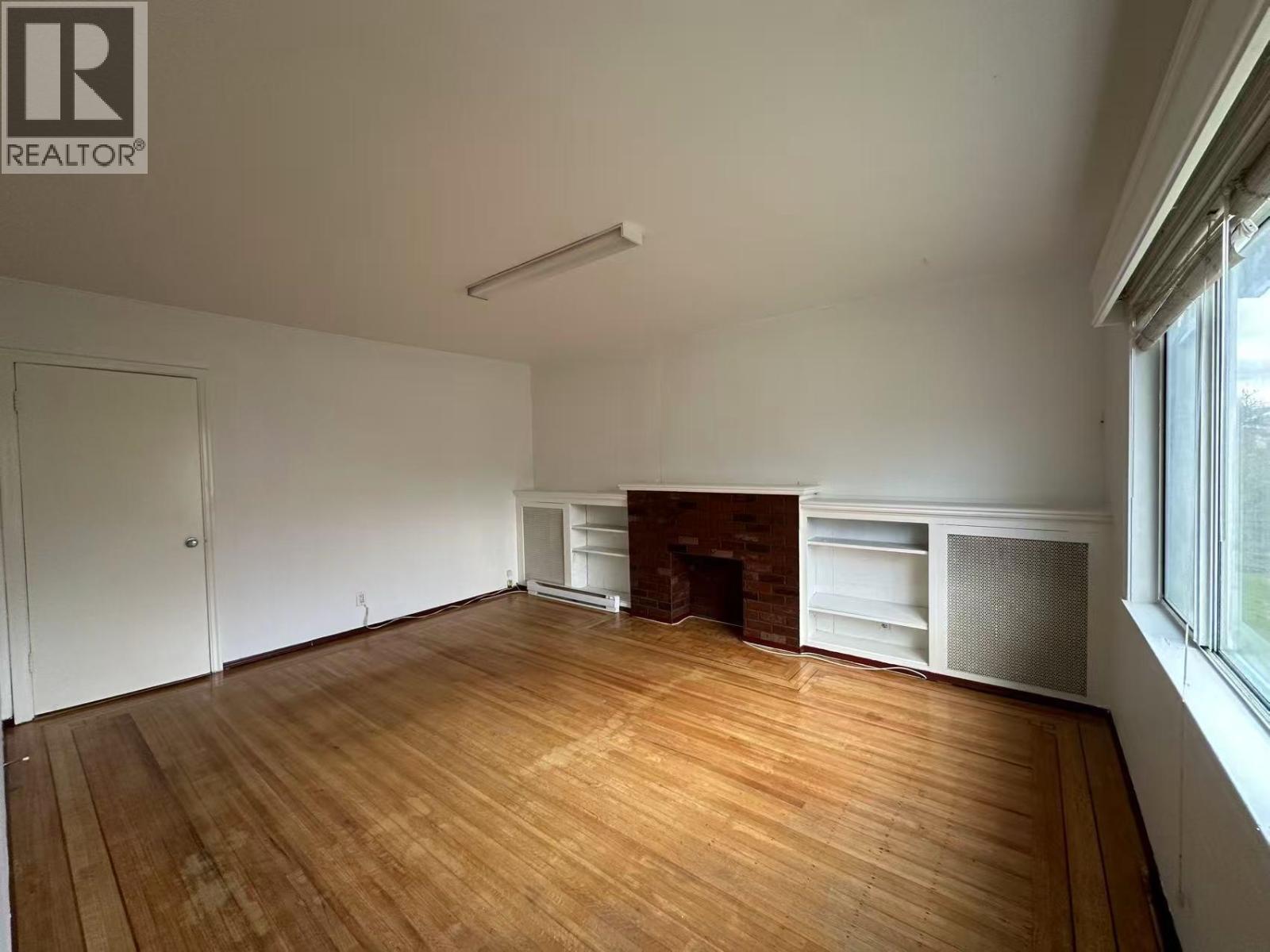 A large empty room with wooden floors and a fireplace.