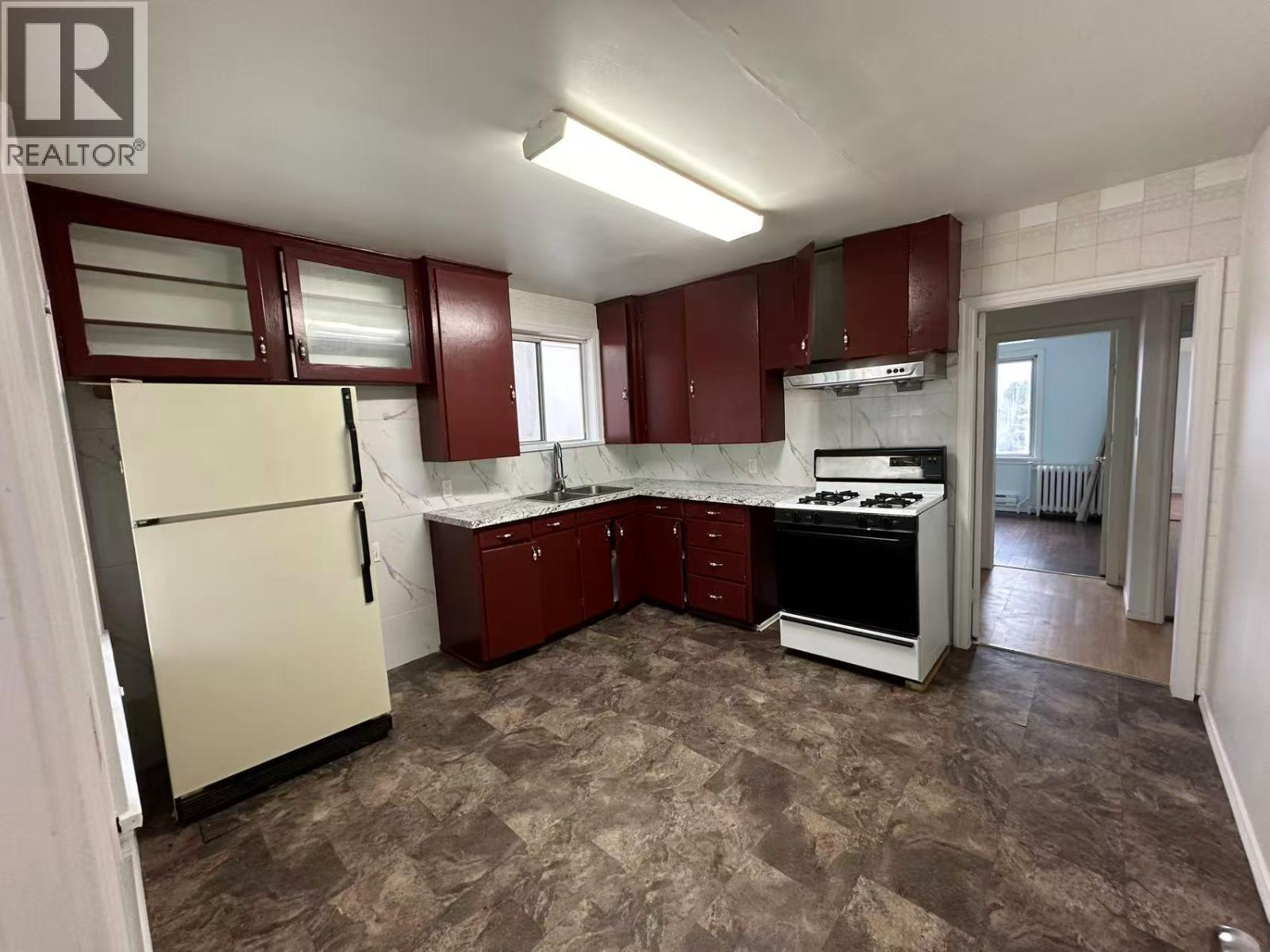 A kitchen with a refrigerator, sink, stove, and cabinets.