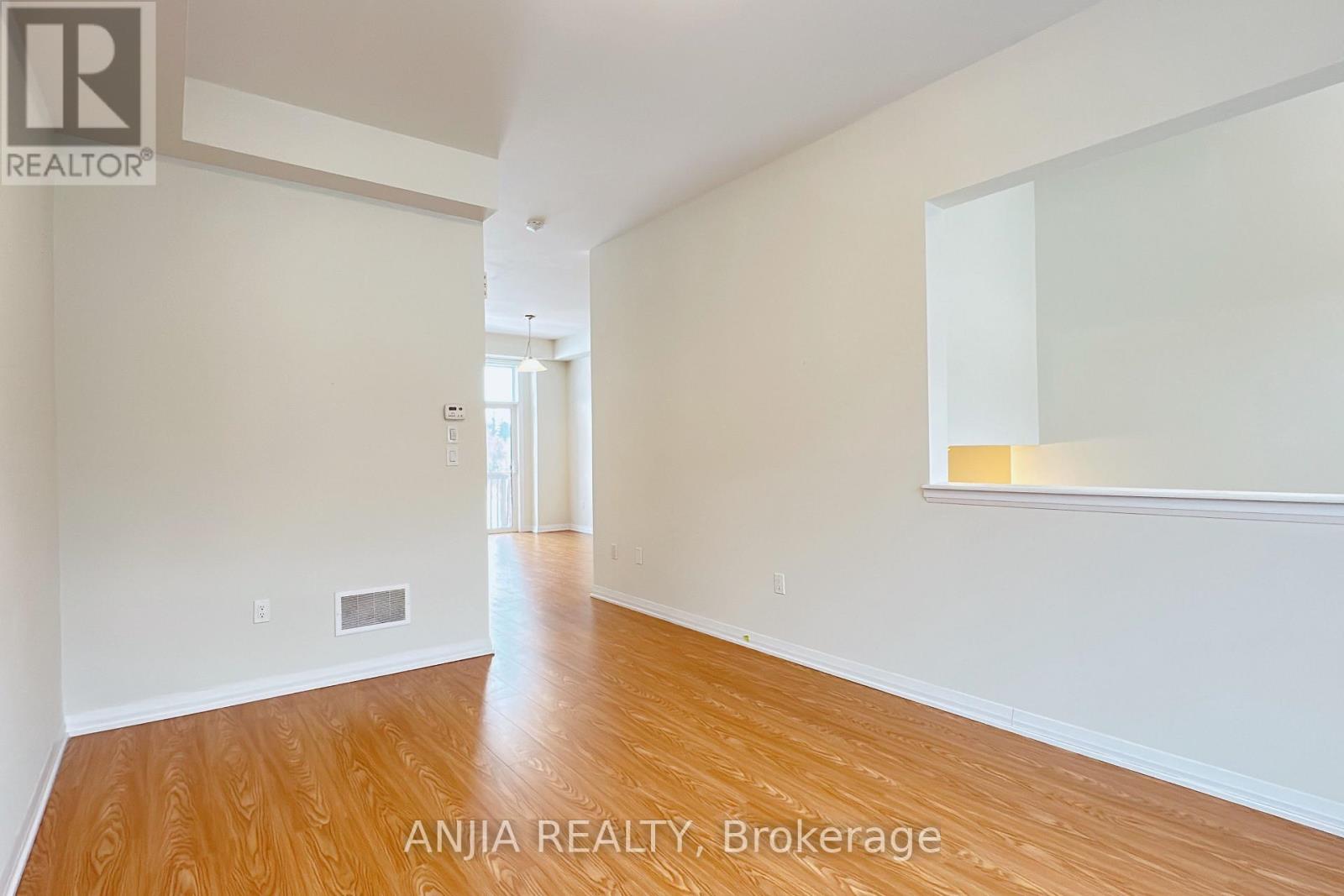 A spacious room with wooden flooring and white walls, with a doorway leading to another room.