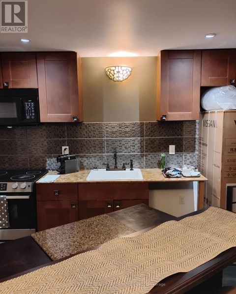 A kitchen with brown cabinets and a black microwave.
