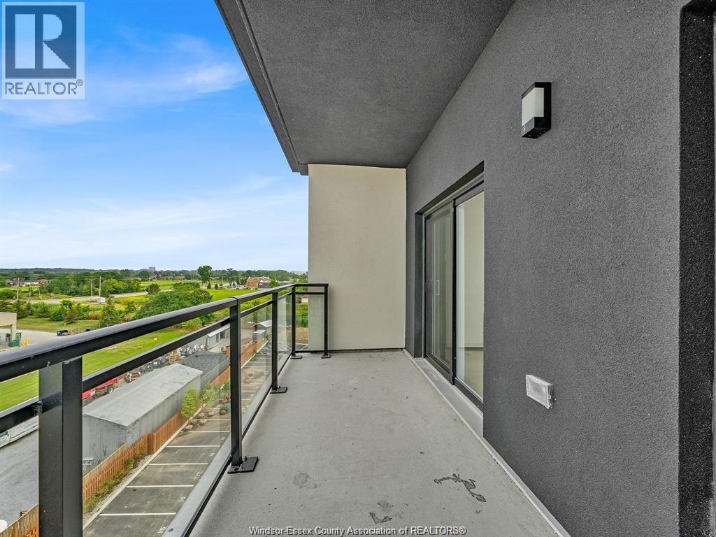 A balcony with a metal railing and a view of a parking lot and trees.