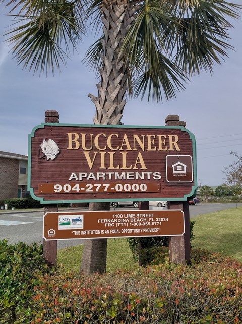 A sign for Buccaneer Villa Apartments with a phone number and address.