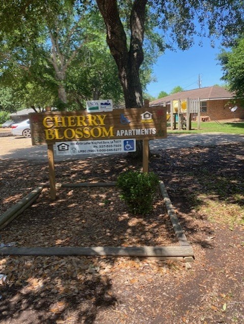 A sign for Cherry Blossom Apartments stands in front of a tree.