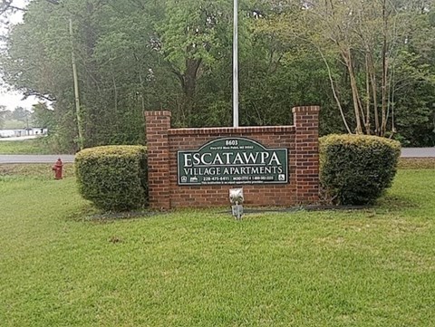 A sign for Escalawpa Village Apartments sits in front of a green lawn.