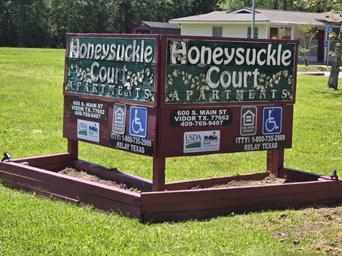 A sign for Honeysuckle Court Apartments is displayed on a grassy area.