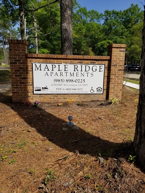 A sign for Maple Ridge Apartments is displayed on a brick pillar.