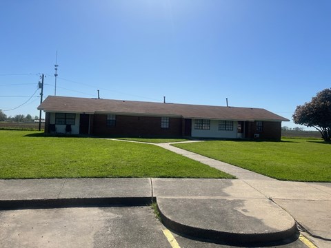 A building with a brown roof and a white door is surrounded by a grassy area and a concrete walkway.
