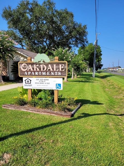 A sign for Oakdale Apartments is in front of a tree.