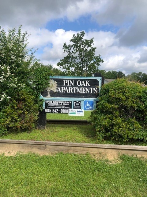 A sign for Pin Oak Apartments with a phone number and a handicap symbol.