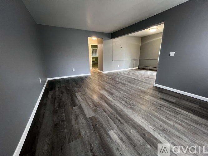 A spacious room with wooden flooring and a doorway leading to another room.