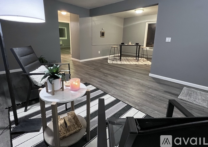 A modern living room with a black and white striped rug, a black chair, a small table with a candle, and a dining table in the background.