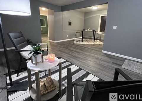A modern living room with a black and white striped rug, a black chair, a small table with a candle, and a dining table in the background.