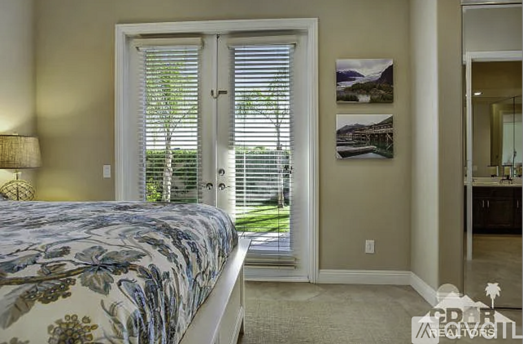 A bedroom with a floral bedspread and a view of a green landscape through the window.