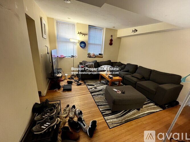 A living room with a couch, a rug, and shoes scattered on the floor.