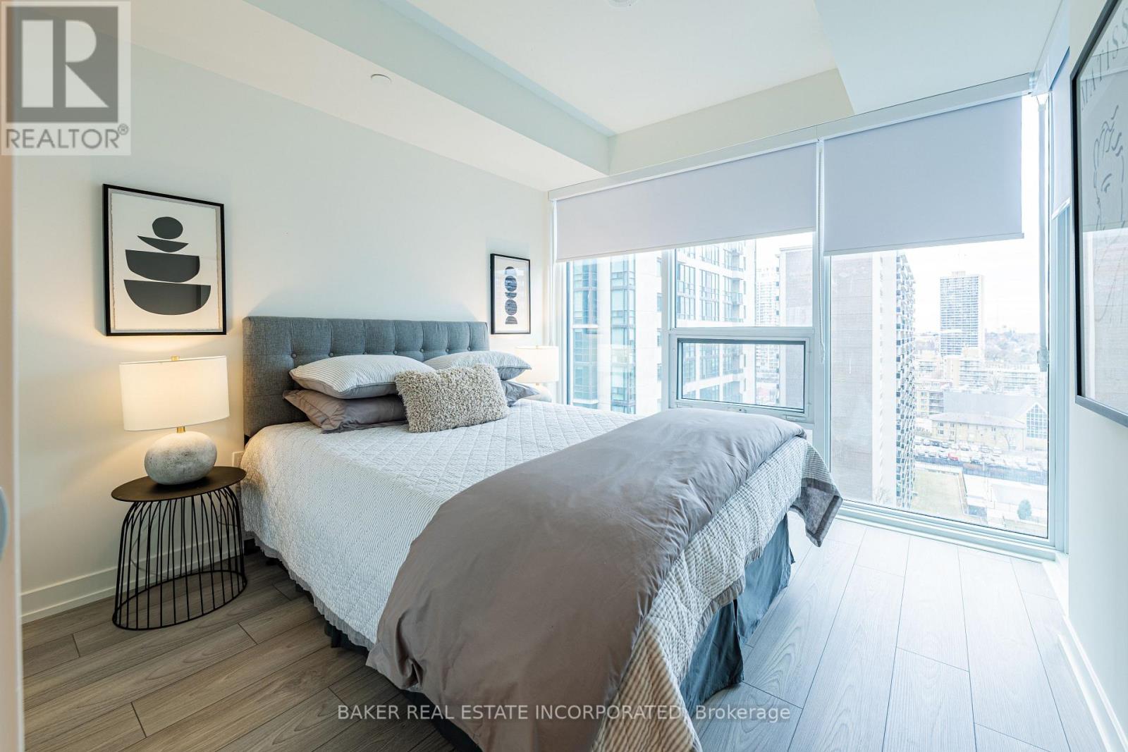 A bedroom with a large bed and a city view through the window.