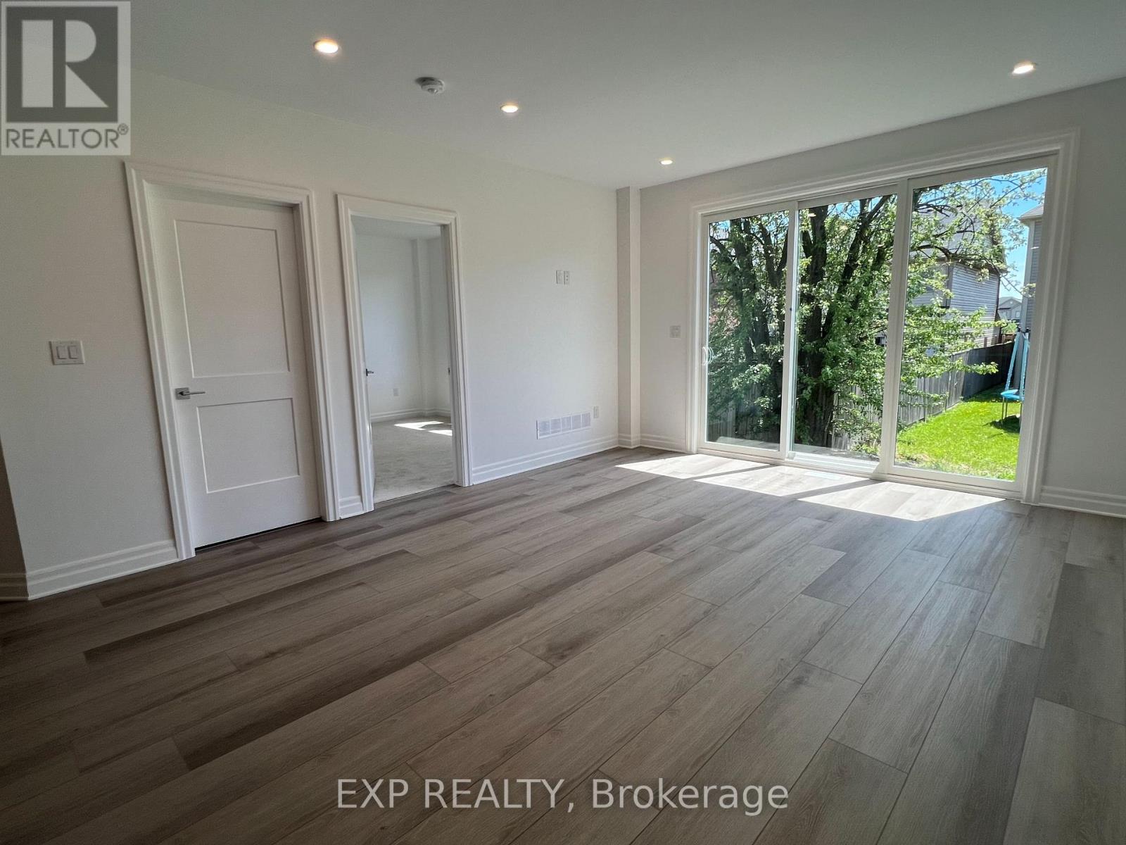 A room with wooden flooring and white walls, with a window showing greenery outside.