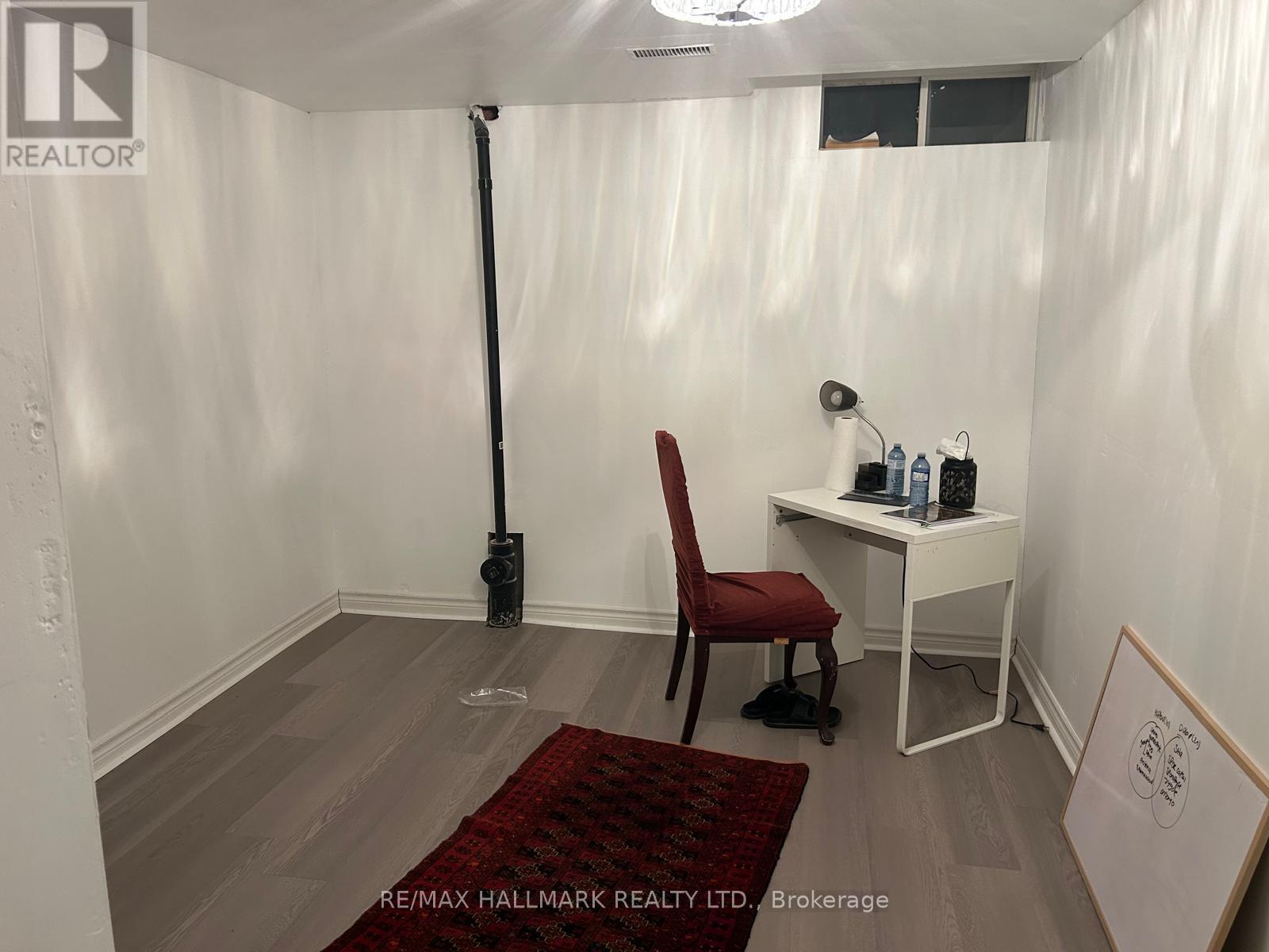 A room with a red chair and a desk with a white chair and a sign that says RE/MAX HALLMARK REALTY LTD Brokerage.
