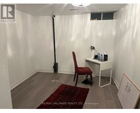 A room with a red chair and a desk with a white chair and a sign that says RE/MAX HALLMARK REALTY LTD Brokerage.