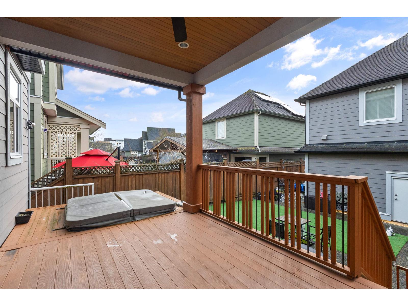 A wooden deck with a hot tub and a red umbrella.