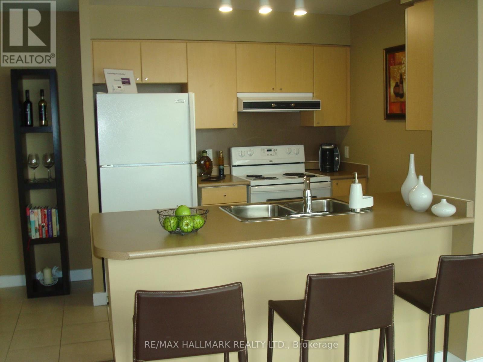 A kitchen with a white fridge, brown chairs and a sink.