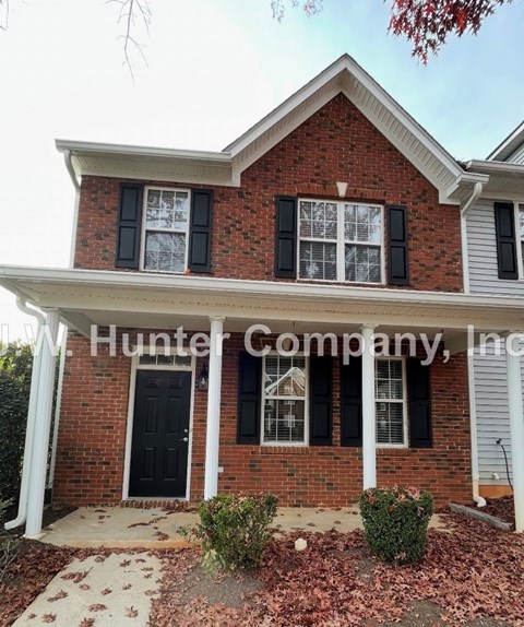 A brick house with a black front door and two windows with shutters.
