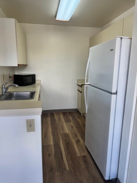 A white refrigerator stands in a kitchen with wood floors and white cabinets.