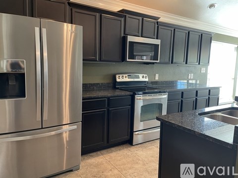A kitchen with black cabinets and a stainless steel refrigerator.