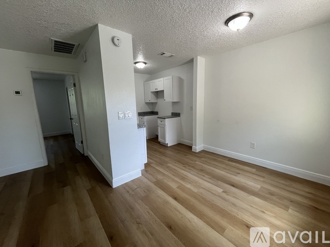 A room with wooden floors and white walls, with a kitchenette in the corner.