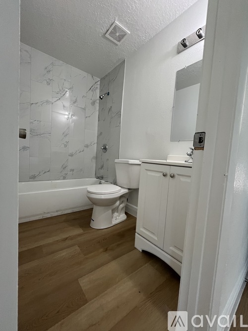 A white bathroom with a marble wall and wooden floor.