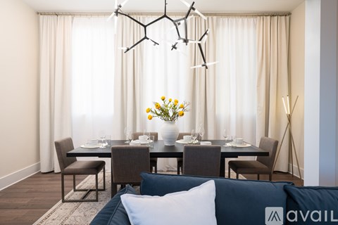 A modern dining room with a dark table and chairs, a chandelier, and a vase of flowers on the table.