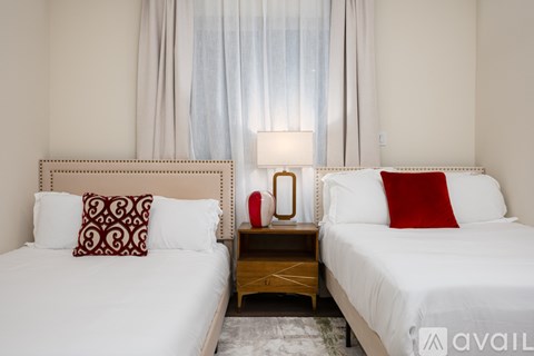 A bedroom with two beds, one with a red pillow and a wooden nightstand with a lamp.