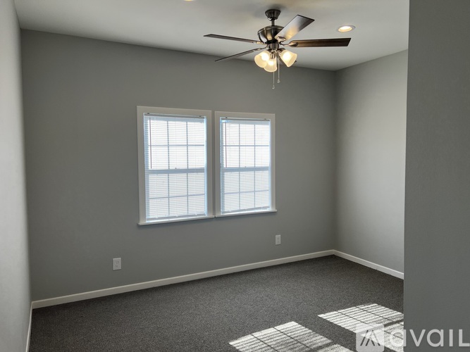 A room with a ceiling fan and two windows.