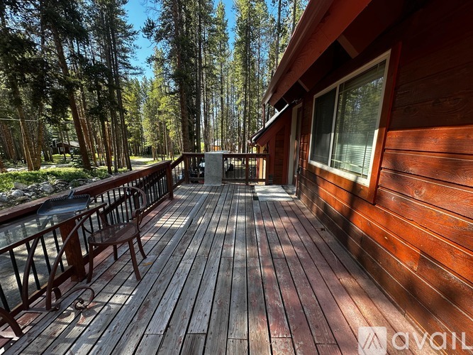 A wooden deck with a railing and a table is surrounded by trees.
