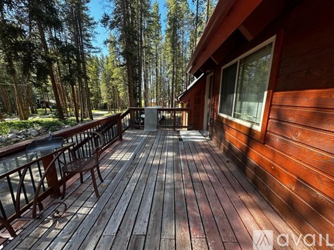 A wooden deck with a railing and a table is surrounded by trees.