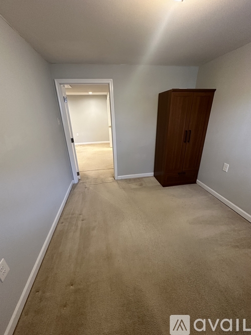 A room with a carpeted floor, a wooden cabinet, and a doorway leading to another room.