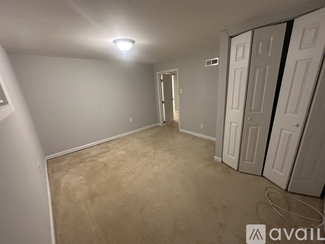 A room with beige carpet and white walls, with a doorway leading to another room.