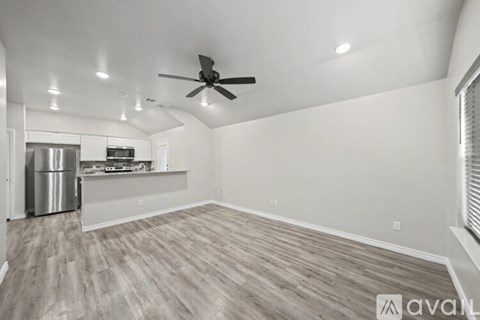 A spacious room with a ceiling fan and a kitchen area with a refrigerator and stove.
