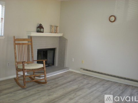 A wooden rocking chair is placed in front of a fireplace in a room.