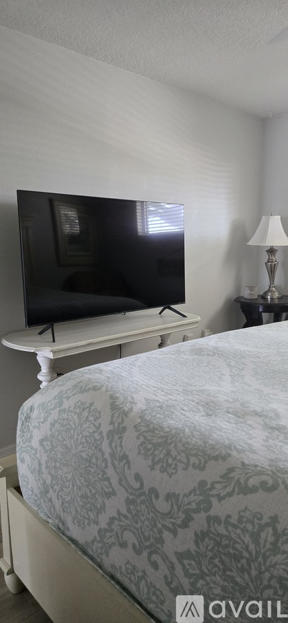 A bed with a patterned sheet sits in a room with a television on a stand.