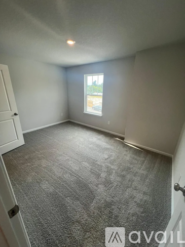 A room with a carpeted floor and a window with a view of trees outside.