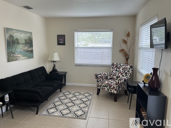 A living room with a black sofa, a patterned chair, and a painting on the wall.