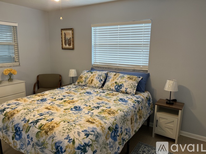 A bedroom with a floral bedspread and a small table with a lamp.